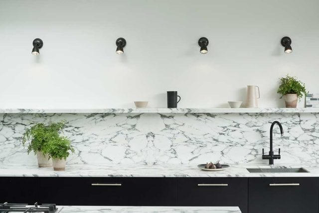 Four separate spotlights on a white wall, above a marble backsplash