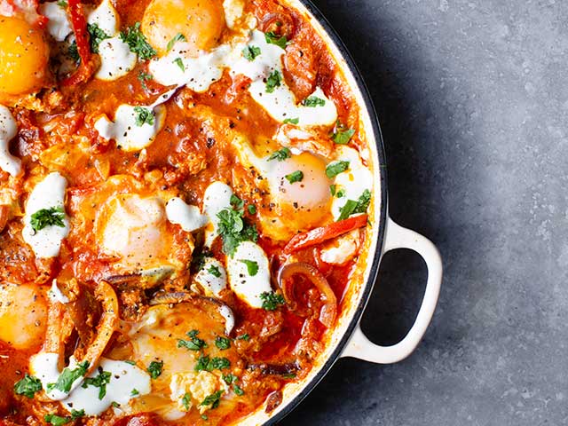 A casserole dish filled with a tomato sauce, peppers, herbs, and poached eggs - Father's Day breakfasts - Goodhomesmagazine.com