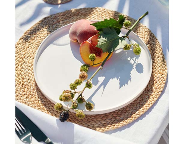 Circular jute placemats on white table linen with peach and foilage on top, goodhomesmagazine.com