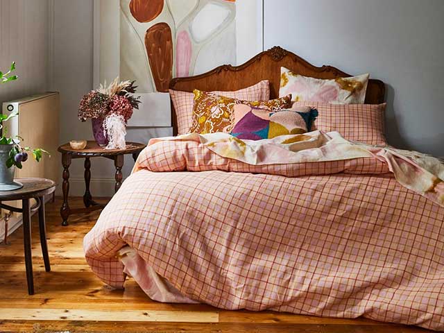 A rustic bedroom setting with an antique bed and headboard, and checked bedding in muted pink and peach tones - Statement bedrooms - Goodhomesmagazine.com