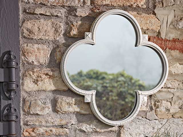 White framed mirror in a quatrefoil shape, hung on a brick wall - Garden mirrors - Goodhomesmagazine.com