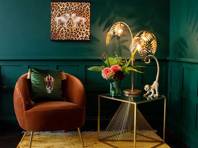 The corner of an emerald green room featuring a burnt orange velvet armchair next to a gold side table that's decorated with ornaments - Earthy tones - Goodhomesmagazine.com