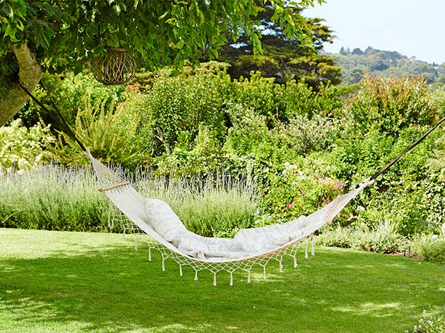 White hammock attached to trees in a grassy garden - 2021 garden furniture - Goodhomesmagazine.com