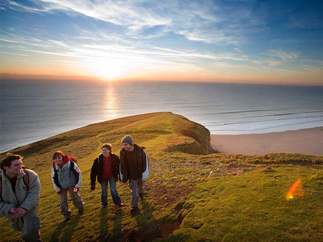 Four people talking on a cliff edge overlooking a sandy bay - UK days out - Goodhomesmagazine.com