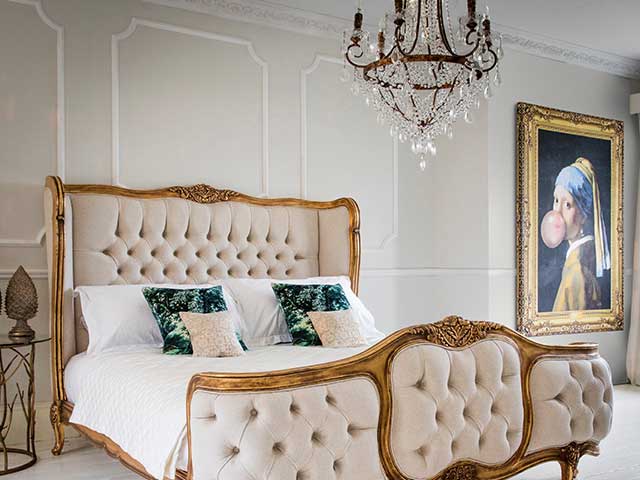A bedroom with a neutral colour scheme, antique-style cream bed, and large iron vintage chandelier with hanging glass droplets - Statement bedrooms - Goodhomesmagazine.com