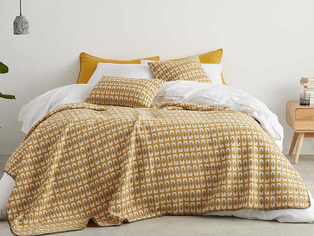 A double bed with white bedding, a patterned mustard throw, and large mustard cushions - Earthy tones - Goodhomesmagazine.com