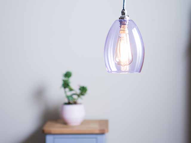 Small purple pendant light hanging from ceiling with houseplant in background