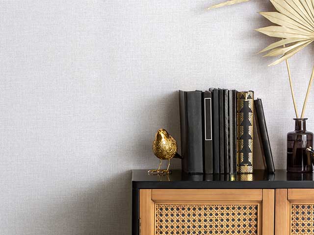 Brown rattan cabinet with black and gold accessories in front of a grey painted wall - Goodhomesmagazine.com