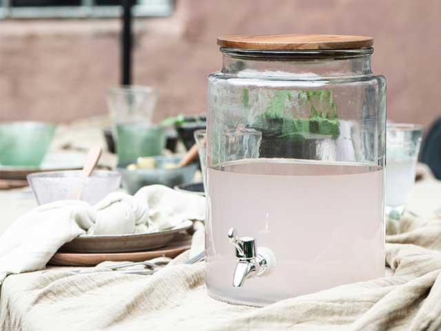 Glass drinks dispenser with a solid wooden lid on a table outside - BBQ week essentials - Goodhomesmagazine.com