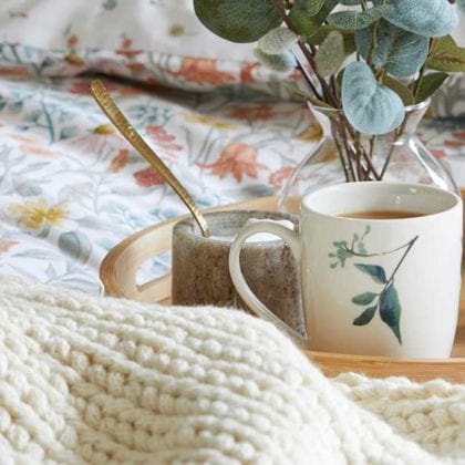 A bed with heritage pattern bedding, a wooden tray with mugs on it, a woven throw, and a burnt orange cushion - Goodhomesmagazine.com