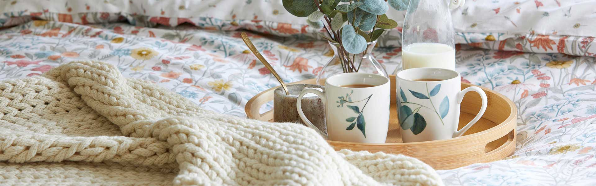 A bed with heritage pattern bedding, a wooden tray with mugs on it, a woven throw, and a burnt orange cushion - Goodhomesmagazine.com