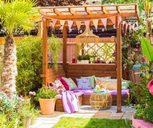 A grassy garden with a pergola that has been decorated wirth bunting, cushions, and blankets - Garden party essentials - Goodhomesmagazine.com