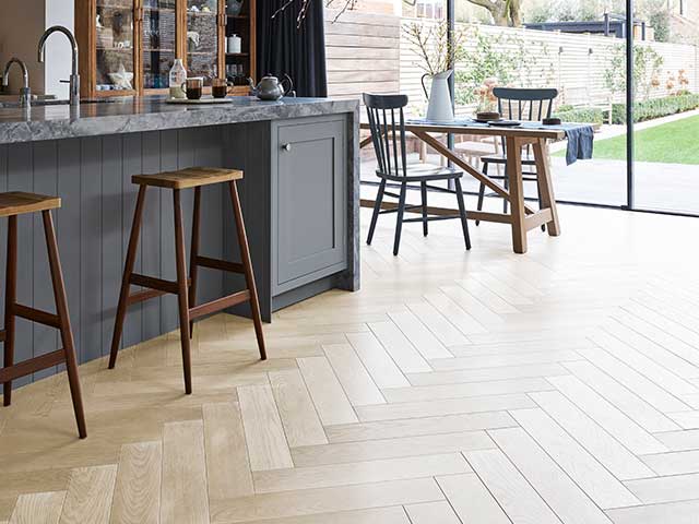 Herrinbone patterned light wooden flooring in a kitchen that has a breakfast bar and wooden table - Flooring trends - Goodhomesmagazine.com