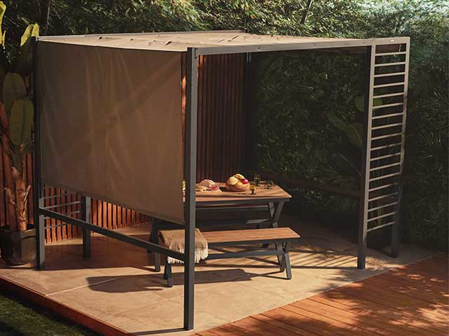Picnic bench under a steel frame pergola with a fabric awning - Garden party essentials - Goodhomesmagazine.com