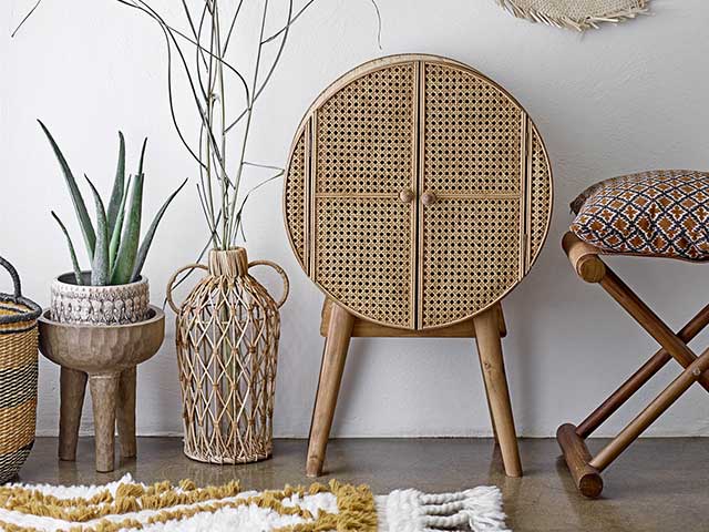 Round wooden and rattan cabinet next to a wooden footstool and some plant pots - Rattan - Goodhomesmagazine.com
