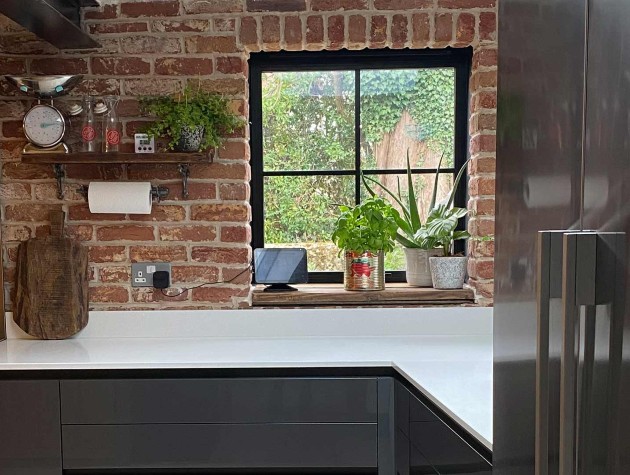 rustic kitchen with exposed-brick wall, brushed-stainless-steel range cooker, dark handleless units with white worktop