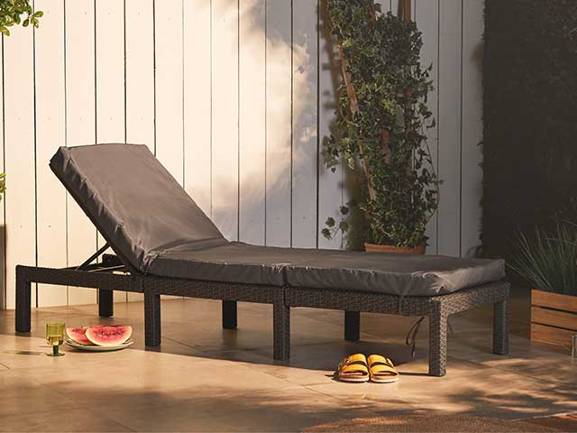 Black rattan sun lounger on the patio with a pair of sandals in front - 2021 garden furniture - Goodhomesmagazine.com