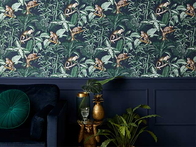 Blue velvet armchair and gold accessories in front of a wall with tropical green wallpaper and navy blue paint - Goodhomesmagazine.com
