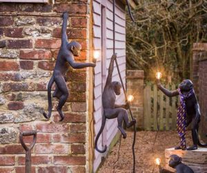 Hanging monkey statues holding garden lights in patio space beside shed with panelled wall