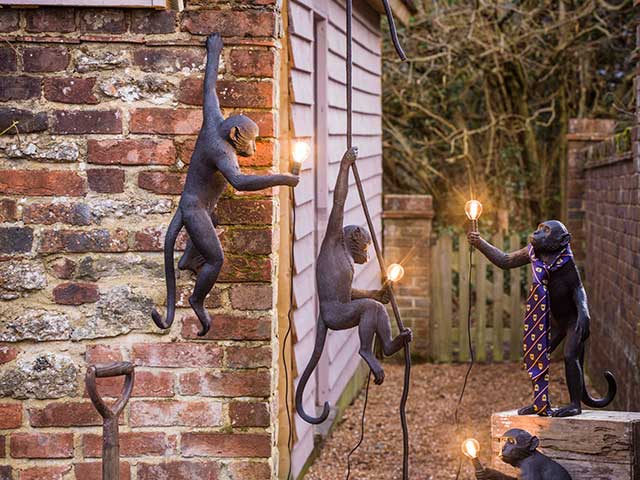 Hanging monkey statues holding garden lights in patio space beside shed with panelled wall