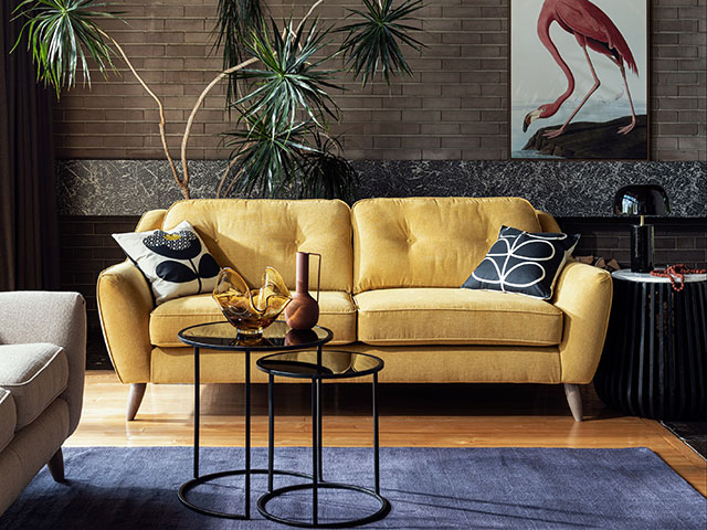 Yellow pincushion two seater sofa in living room with blue rug and black side table