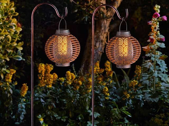 Garden lanterns overhanging on metal poles with bushes and foliage in background