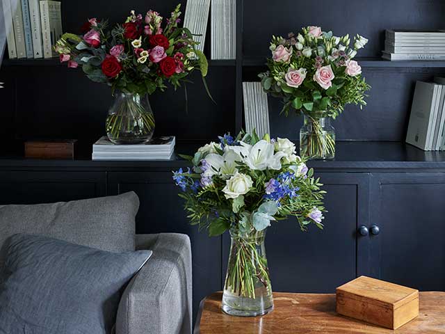 Three bouquets of flowers in red, pink and white in glass vases displayed in living room