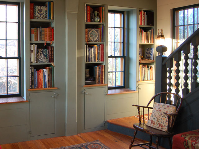 Pale green painted hallway with bespoke shelving and a wall filled with books by Studio Killian Dawsoon