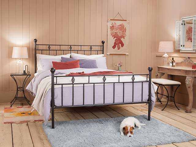 Victorian-style black iron bed frame with a dog on a rug in front of it - Iron beds - Goodhomesmagazine.com