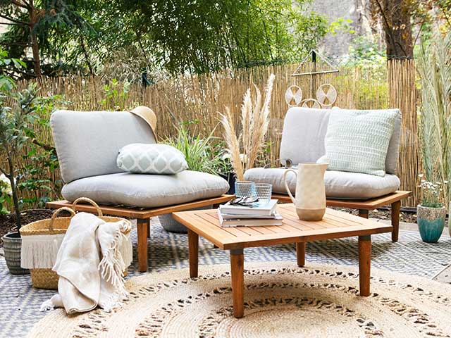 Circular woven natural minimalist outdoor rug with wooden coffee table and slingback chairs with grey cushions
