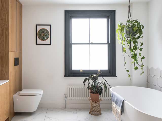 Large bathroom with freestanding porcelain bath and toilet, wooden furniture and plenty of foilage both hanging and on the tiled floor in this Melbourne inspired home