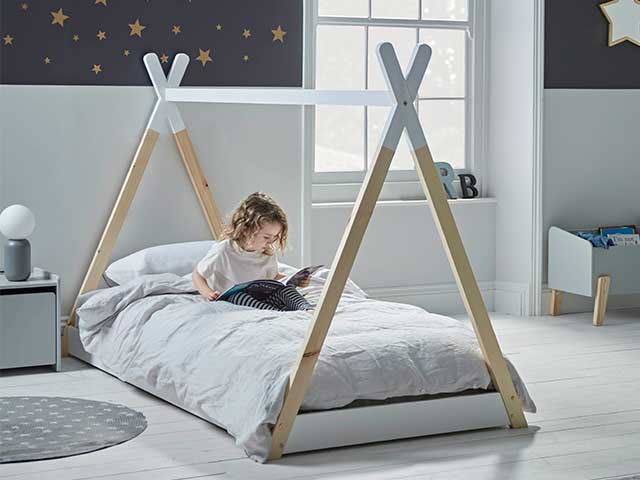 A small child sitting on a bed with a tipi-shaped wooden frame - Children's bedroom furniture - Goodhomesmagazine.com