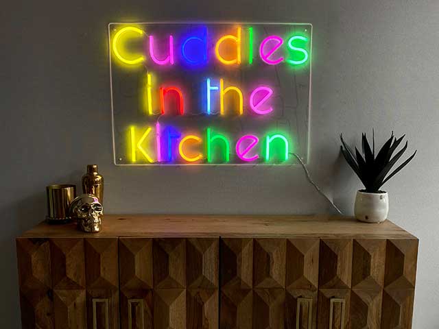 Multicoloured 'Cuddles in the Kitchen' neon sign above a side table - neon lights - Goodhomesmagazine.com