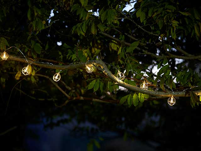 Copper caged string fairy lights hung outdoors between trees - Outdoor Cinema - Goodhomesmagazine.com