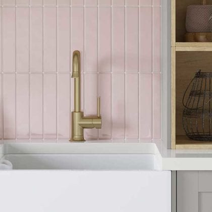 A deep white Belfast sink with a gold tap in front of a pink tiled backsplash - Utility room ideas - Goodhomesmagazine.com