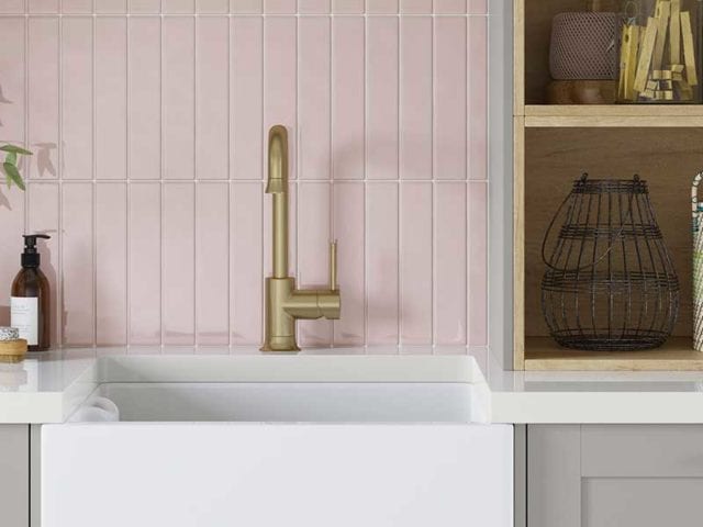 A deep white Belfast sink with a gold tap in front of a pink tiled backsplash - Utility room ideas - Goodhomesmagazine.com