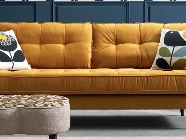 Yellow pincushion sofa with footstll and navy panelled wall behind