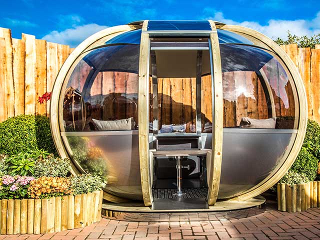 small glass garden pod surrounded by a floral bed