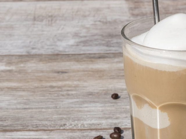 iced coffee in glass with coffee beans scattered on wooden surface