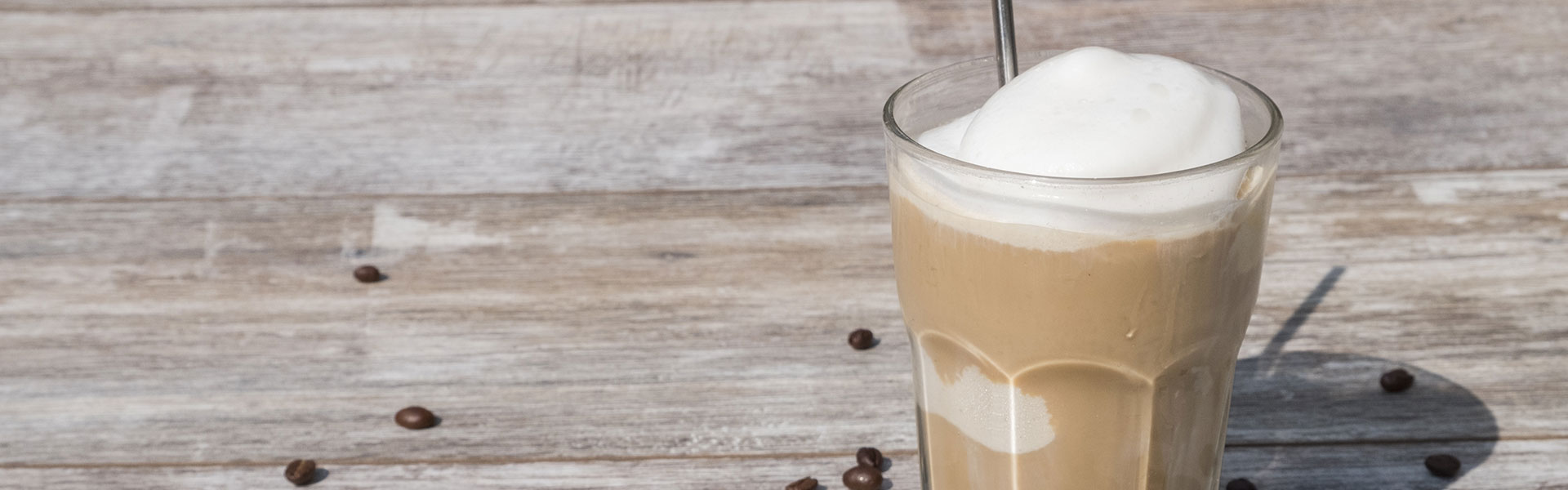 iced coffee in glass with coffee beans scattered on wooden surface