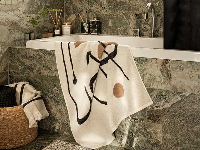 Ceramic marble grey bath tub with patterned cream towel hanging over side