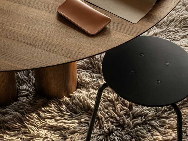 Fluffy rug below wooden circular coffee table and black stall with metal legs