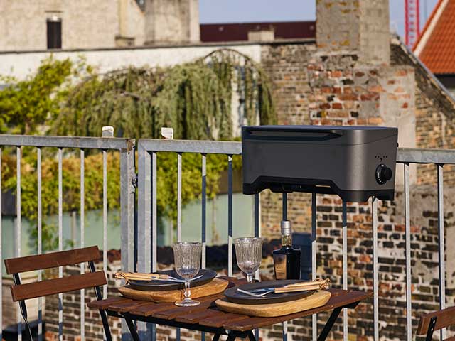 Electric BBQ on railings of balcony and wooden table and chairs with plates and glasses ready to serve