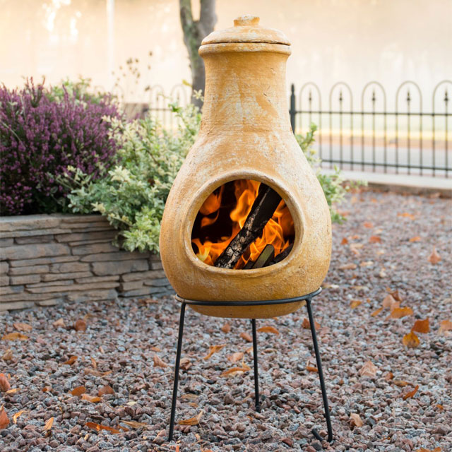 traditional french-style chiminea in mottled beige/yellow with black legs on a gravel garden