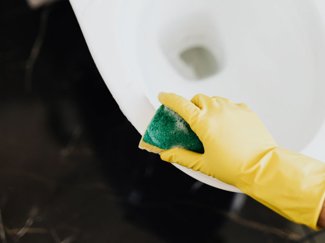 Cleaning the toilet wearing yellow rubber gloves