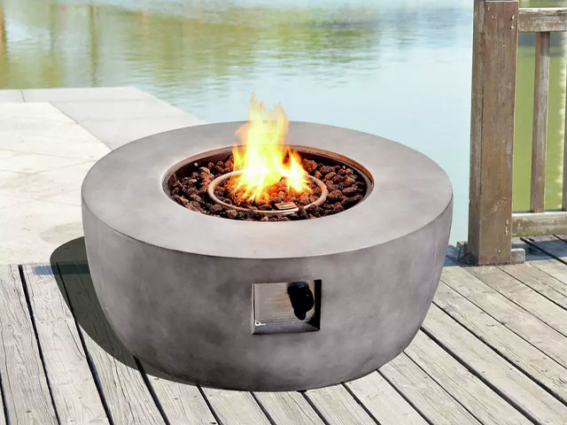 round concrete garden fire pit with lava rocks on a decked patio terrace next to a lake
