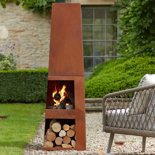 tall, narrow rusty wood burning chiminea with log store