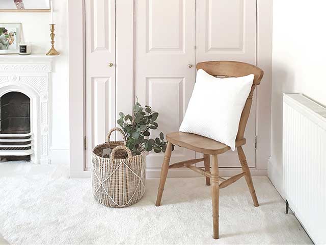 Wooden chair with white cushion and wicker basket with plants by the side, cream carpet and pink panelled doors 