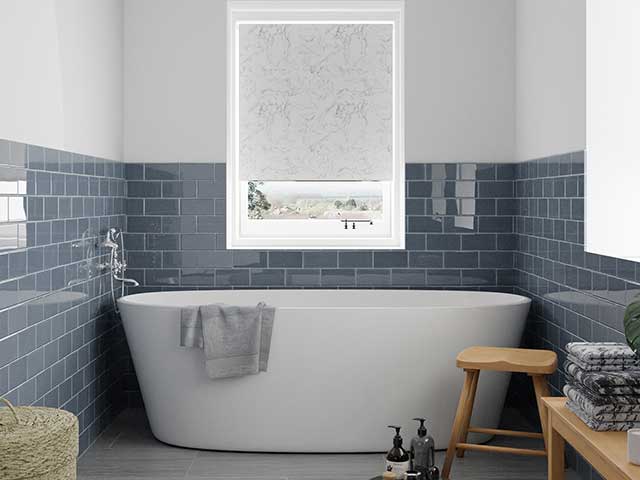 Marble roller blind above freestanding bath tub in blue and white tiled room