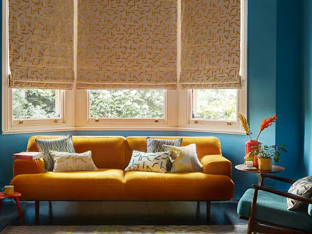 Roller blinds in blue living room with mustard sofa and scatter cushions